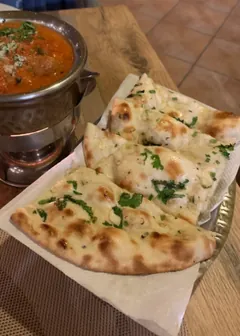 Garlic naan beside a curry in a copper pot