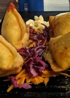 Four samosas on a slate with red cabbage and carrot