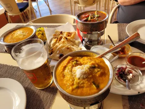 A table with korma, pappadums, chutneys and a glass of beer